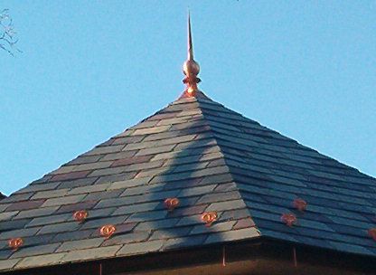 Pointed slate rooftop with a finial against a blue sky