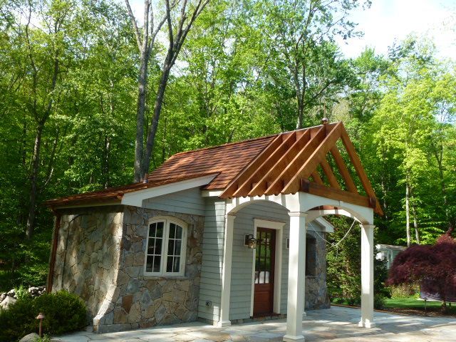 Small stone cottage with a copper roof and white porch in a wooded garden