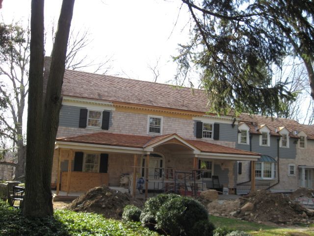 Two-story house with a porch, tan siding, red roof, and trees in front