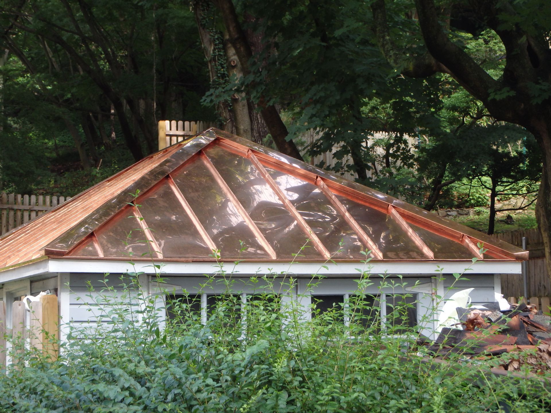 House with a damaged copper roof surrounded by trees and overgrown greenery