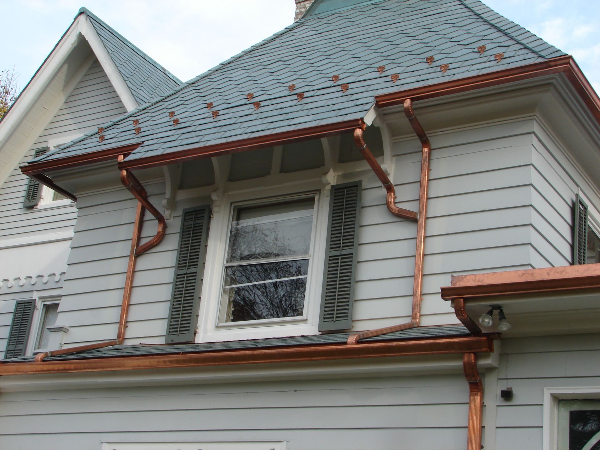House exterior with gray siding, steep roof, and rusty red gutters around a dormer window