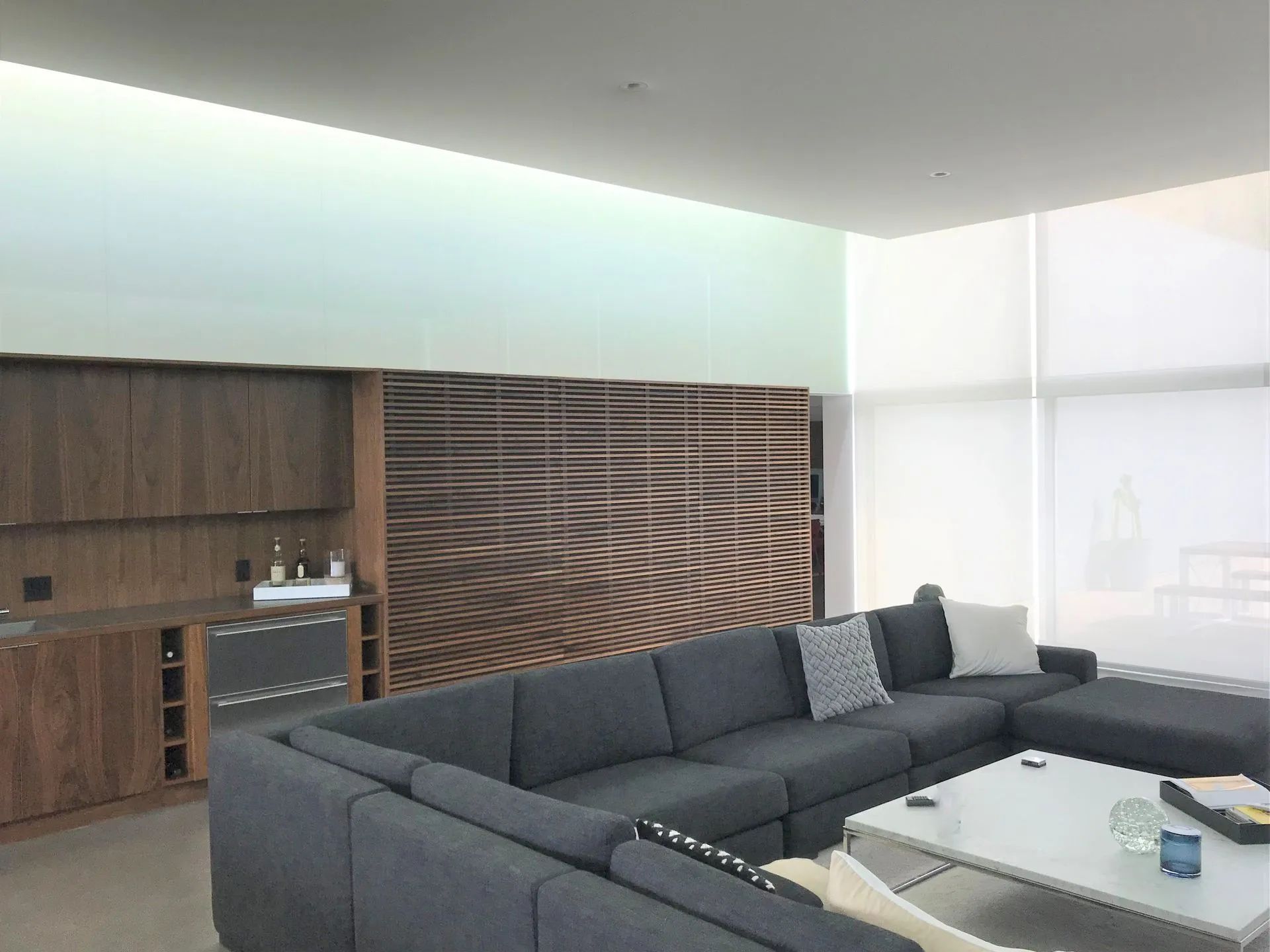Modern living room with gray sectional sofa, glass coffee table, and wood-paneled wall unit.