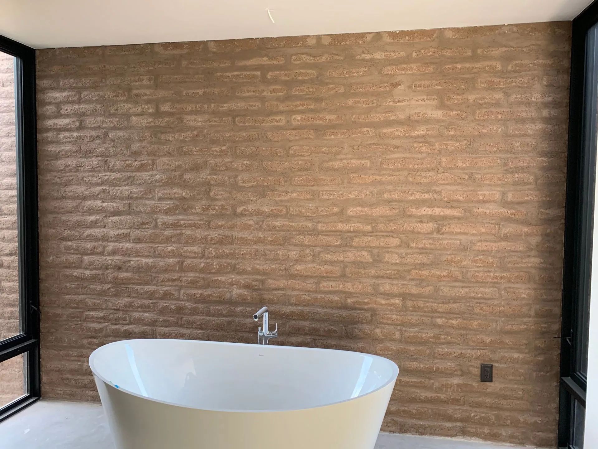 Modern bathroom with a freestanding white tub, sink, and brick-pattern accent wall.