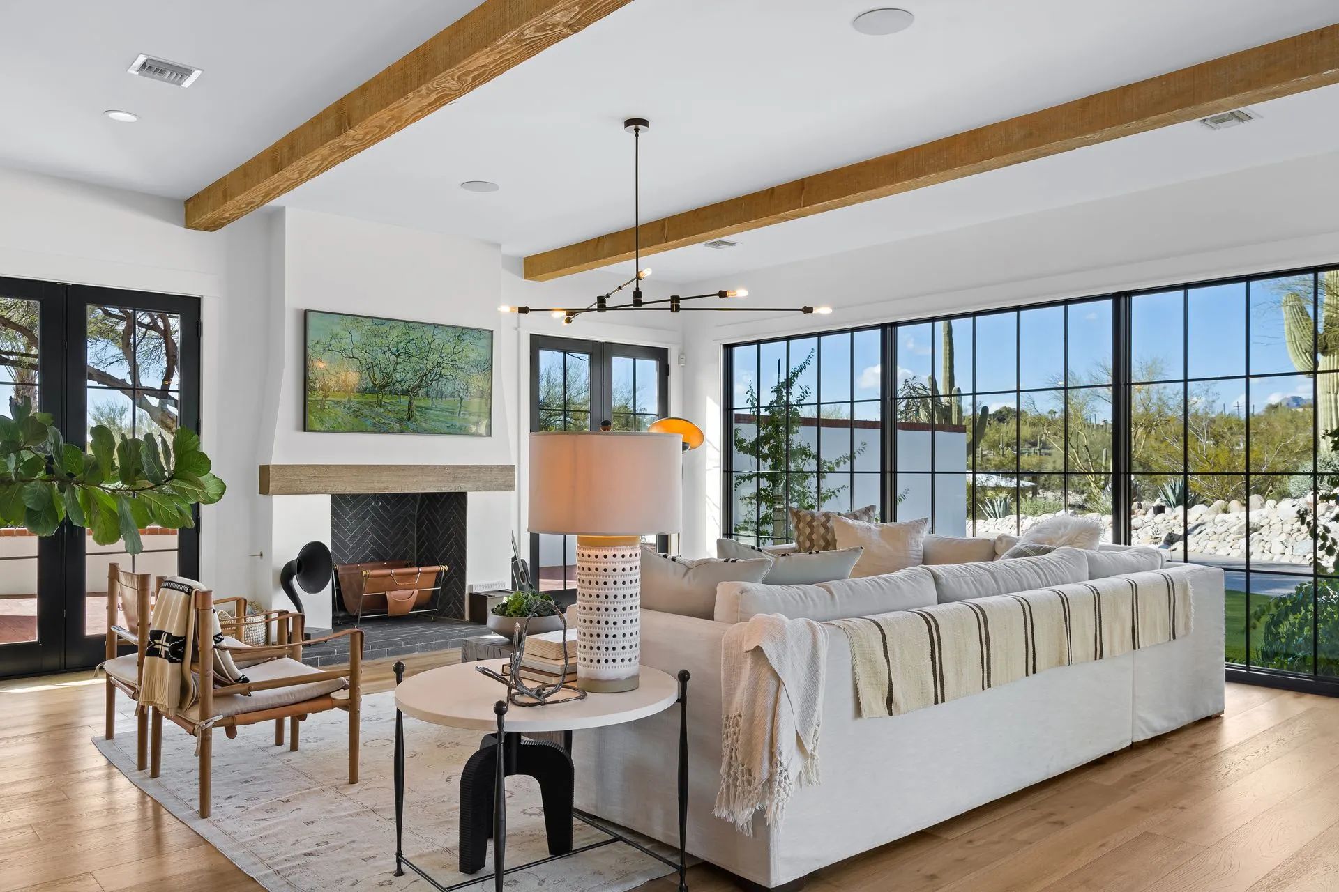 Bright modern living room with white sofas, fireplace, wood beams, and large windows overlooking water.