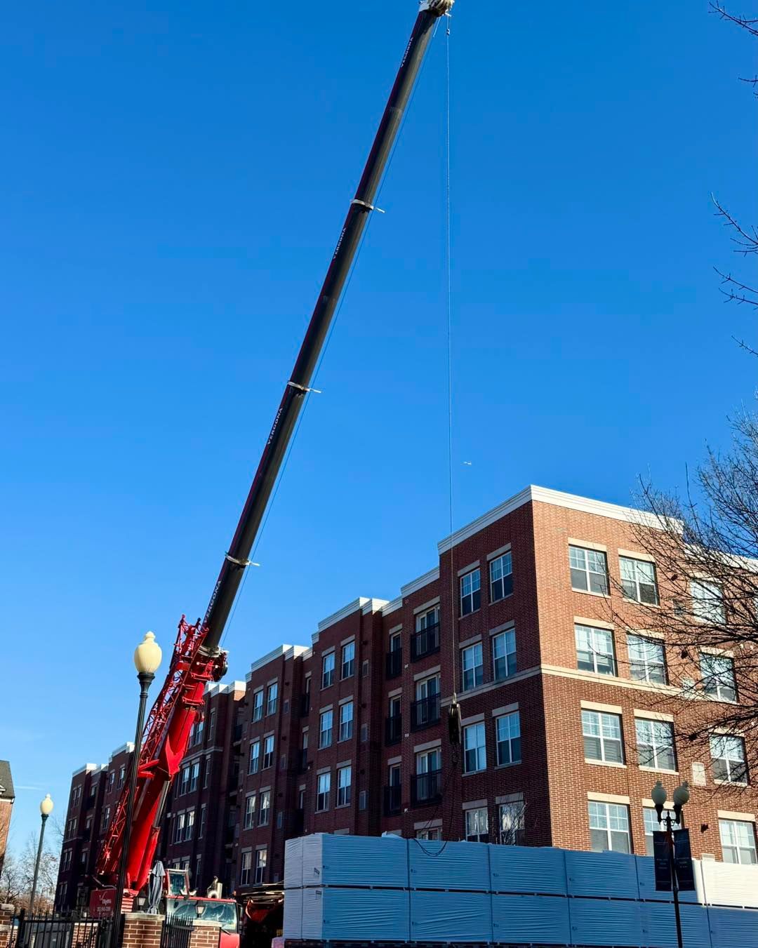Crane lifting materials near a brick apartment building under a clear blue sky.