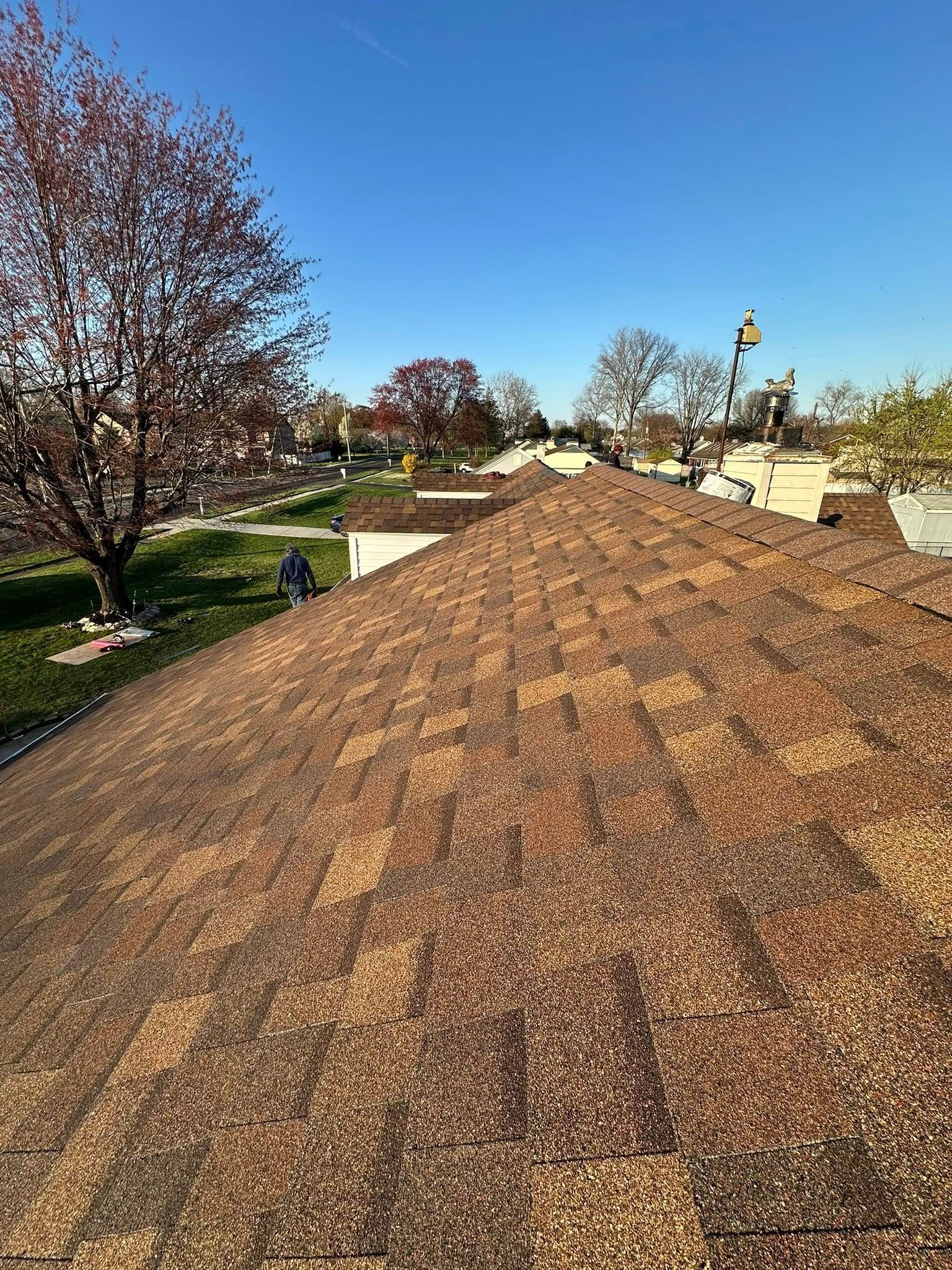 Roof under construction; workers on rooftop, surrounded by shingles, blue sky.