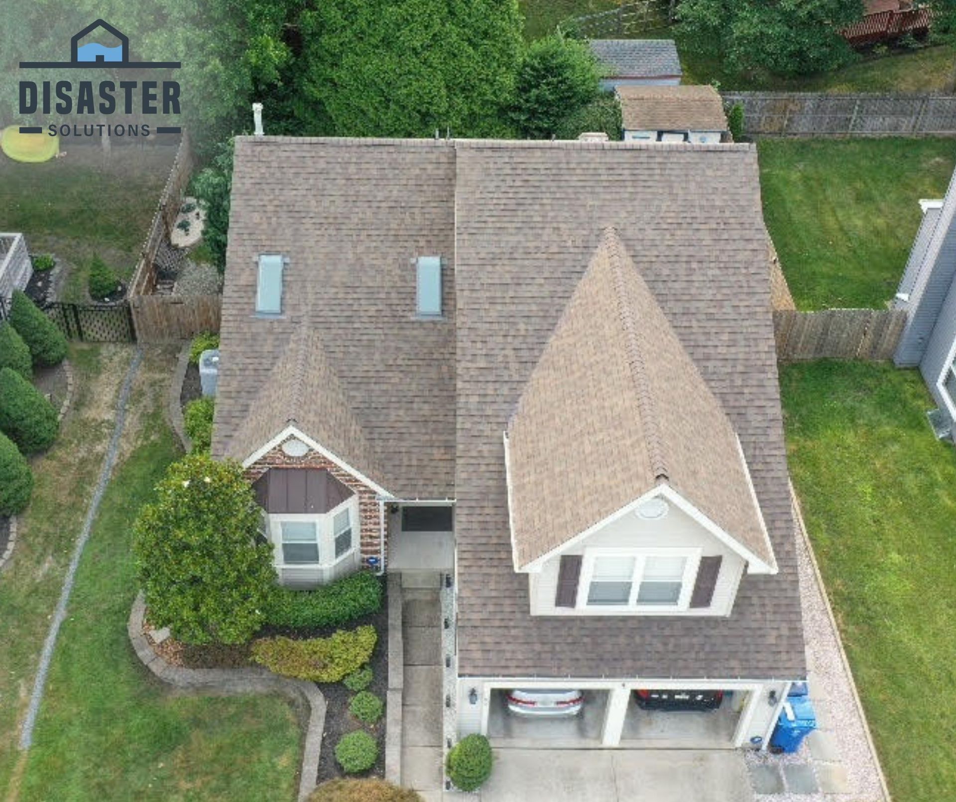 Overhead view of a house with a brown roof and a two-car garage. Lush green lawn and bushes surround the home.