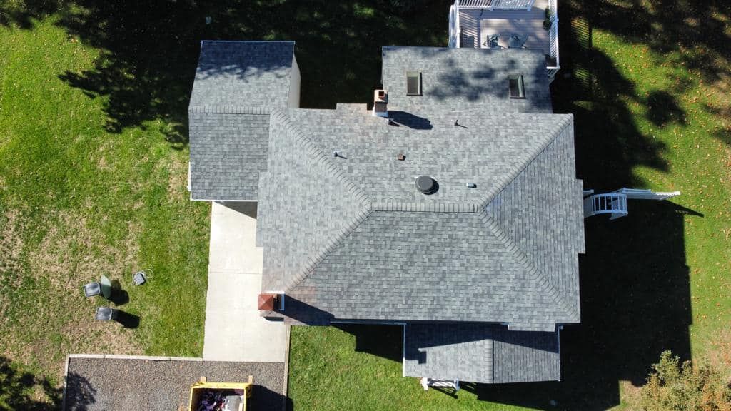 Aerial view of a gray-shingled house with green lawn, a driveway, and a small shed.