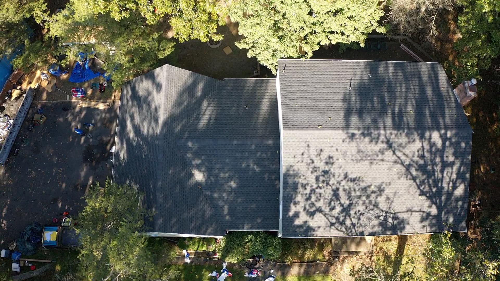 Overhead view of a house with a dark gray roof surrounded by trees and a messy yard.