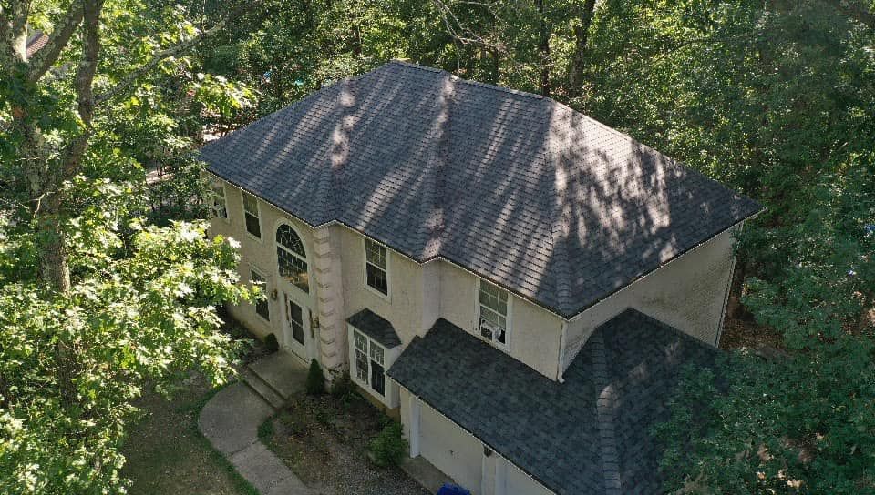 Two-story house with dark roof surrounded by green trees.