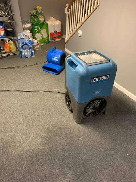 Blue dehumidifier and air mover on gray carpet in a basement.