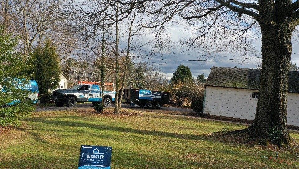 Truck parked on a grassy yard, with equipment, a small building and bare trees under a cloudy sky.