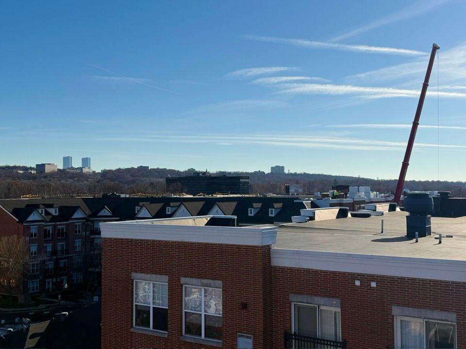 Rooftop view of buildings on a sunny day. A long red crane extends into the blue sky.