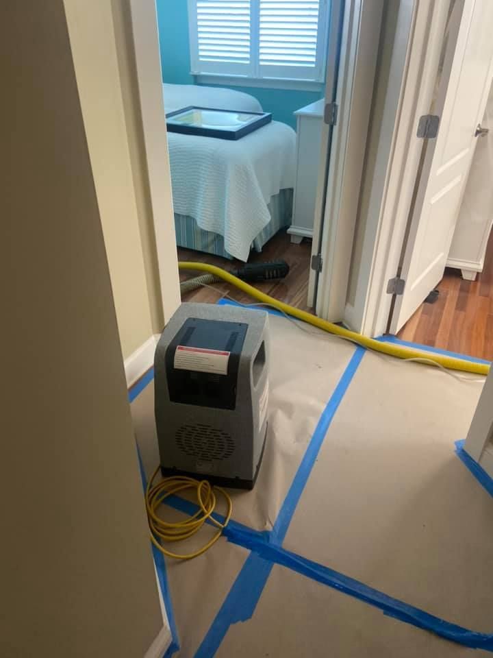 Dehumidifier on protective paper in doorway; bedroom with bed in background. Yellow hose and cord.