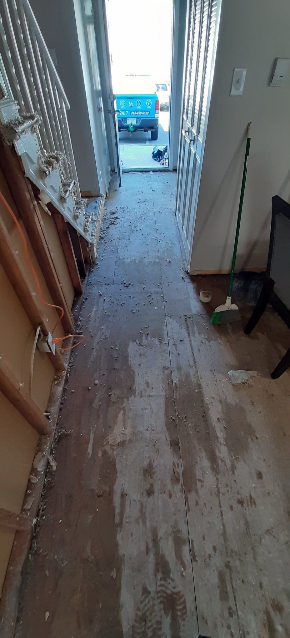 Hallway under construction, door open to outside, exposed floorboards, stairs on left side.