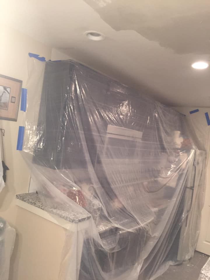 Kitchen cabinets and appliances covered in plastic sheeting, taped for protection during renovation.