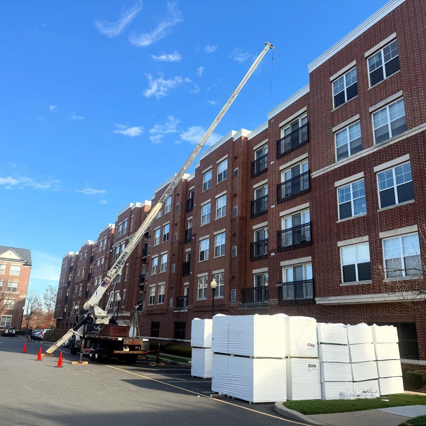 A crane lifting materials to a brick apartment building under a blue sky.