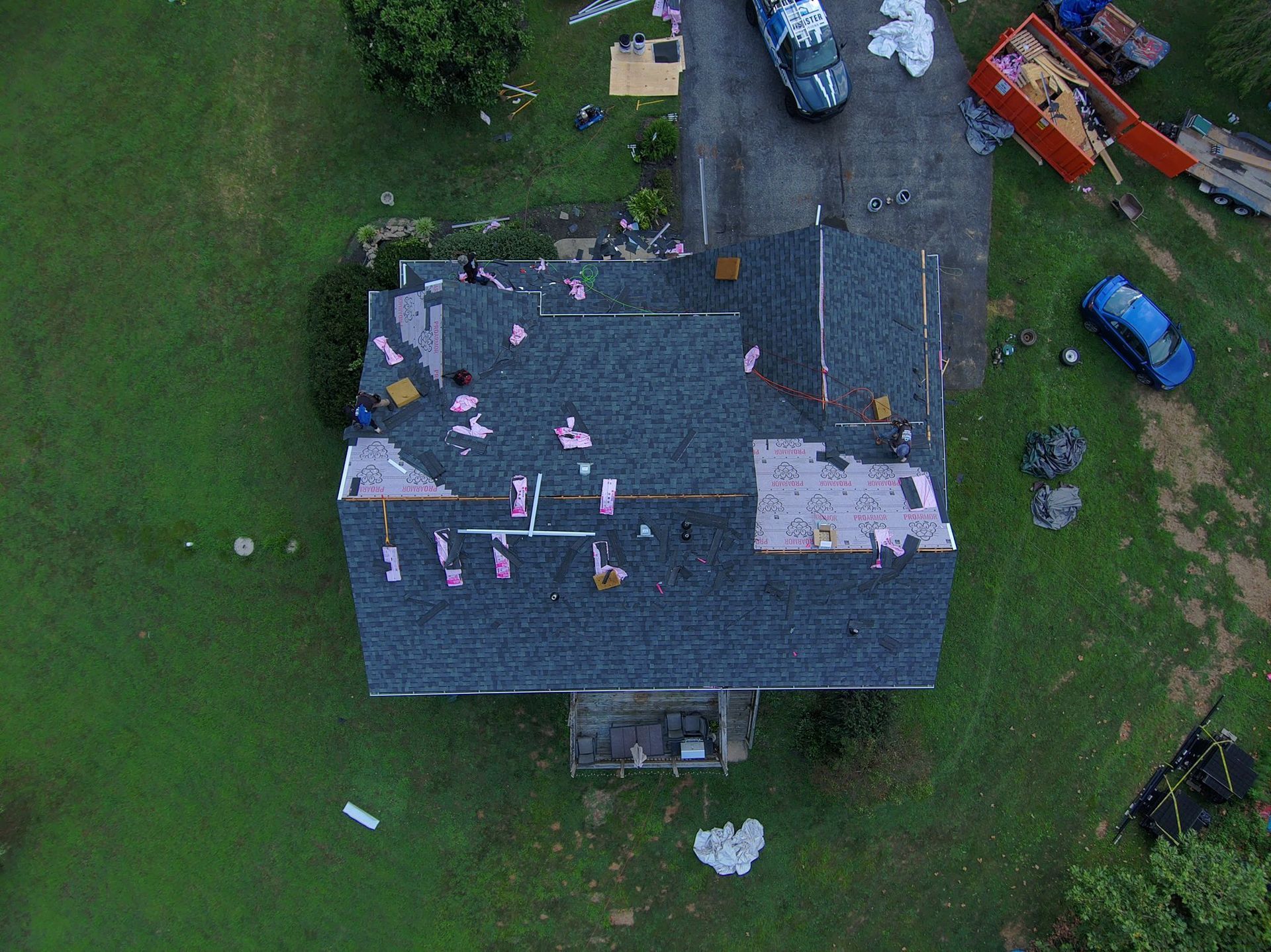 Overhead view of a house with a damaged roof, surrounded by green grass and construction vehicles.