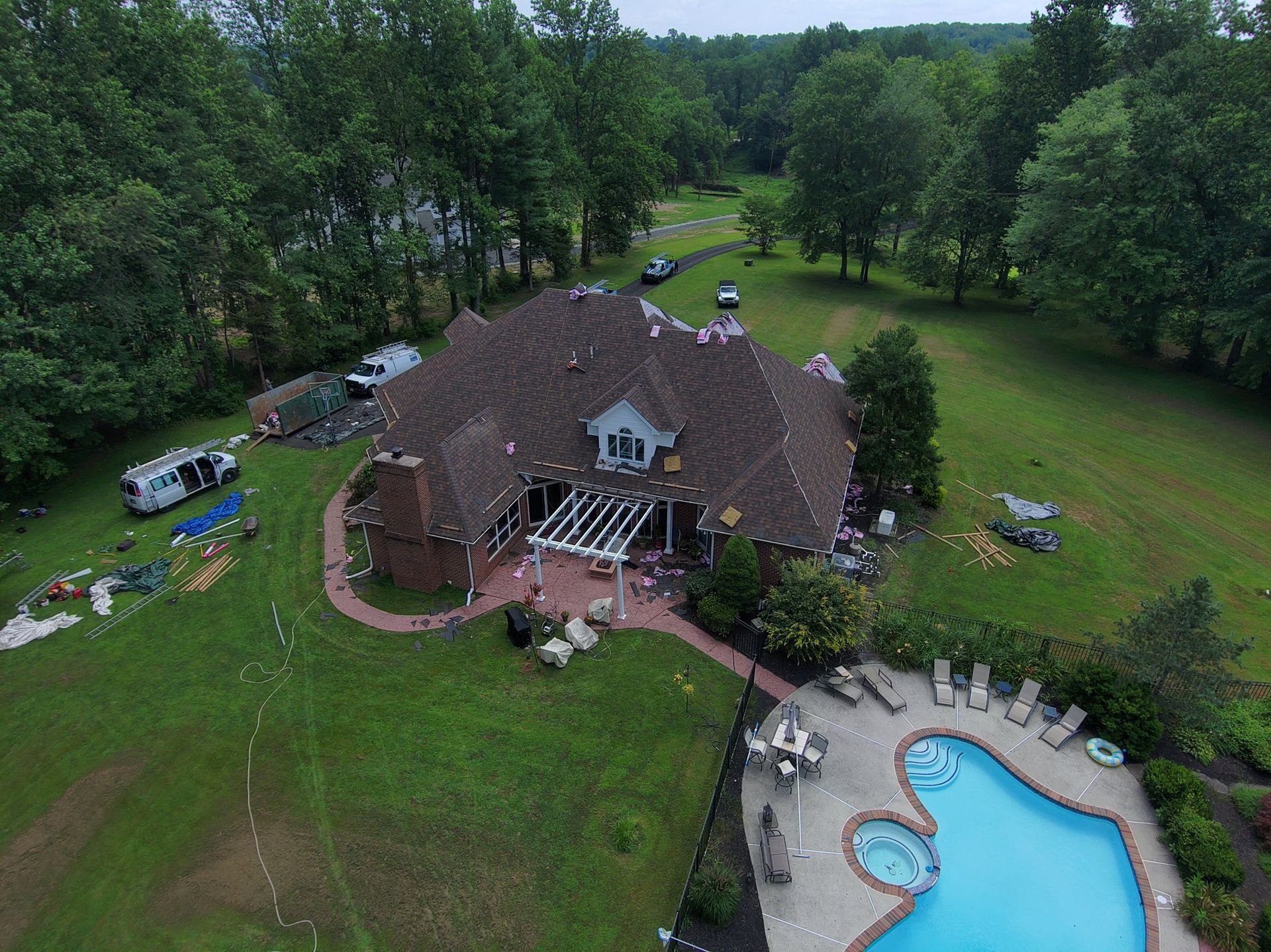 Aerial view of a large house with a pool and lush green lawn, surrounded by trees.