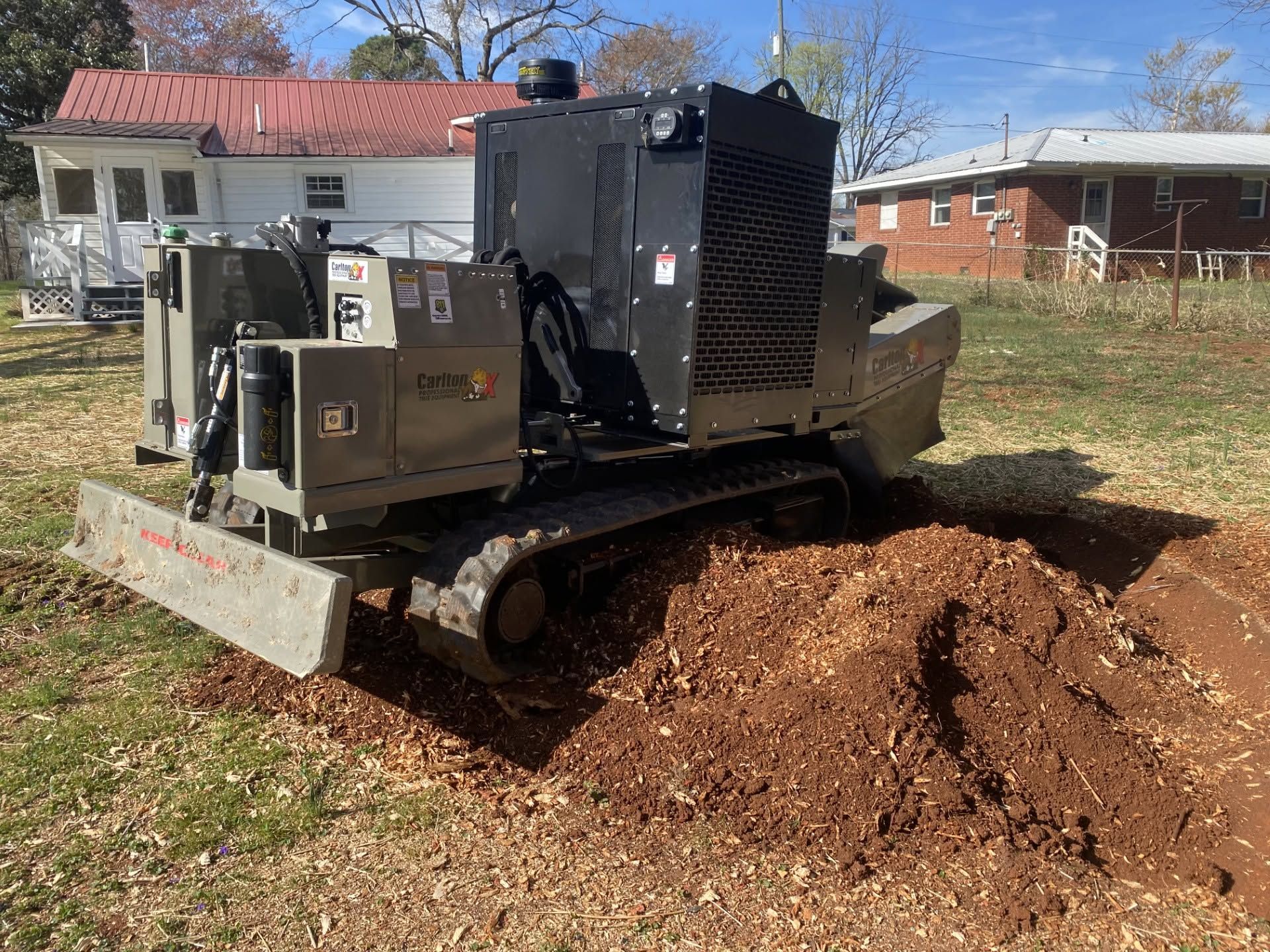 Tracked mulch blower machine spreading wood chips in a yard near houses