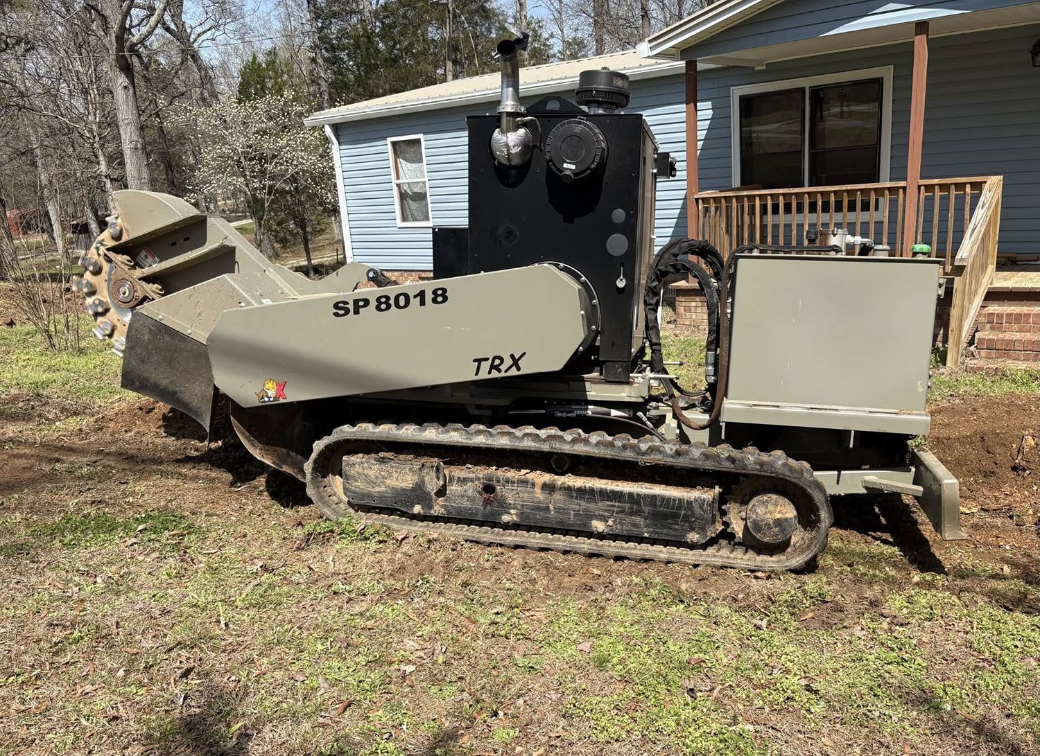 White tracked construction machine parked beside a house in a grassy yard