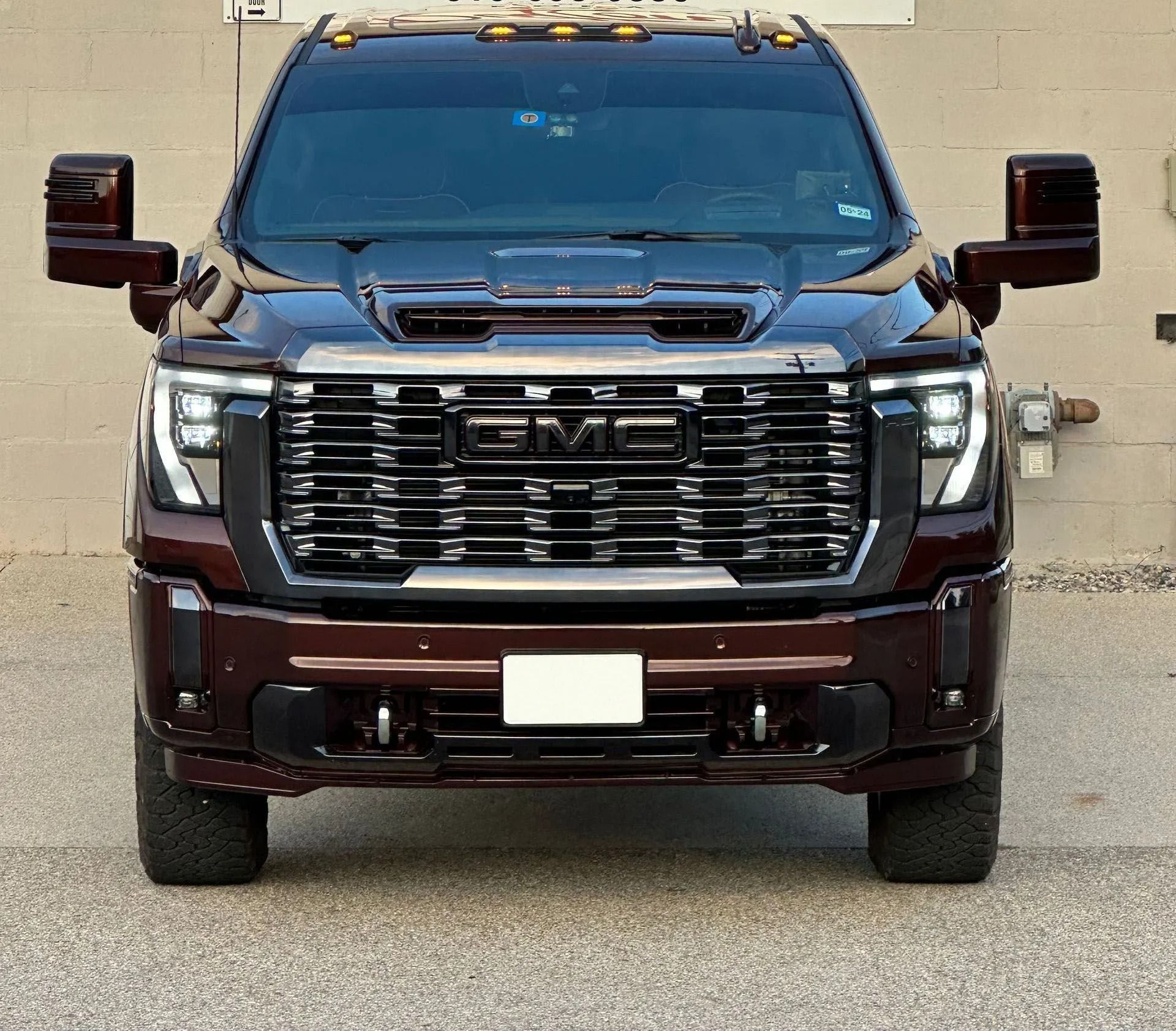 Front view of a dark maroon GMC pickup truck with large grille and tow mirrors parked outdoors