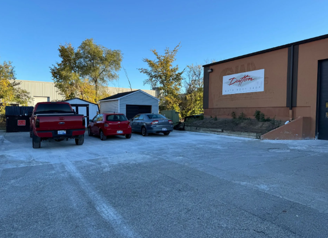 Parking lot with red and gray vehicles beside a tan building with a sign, near trees at sunset