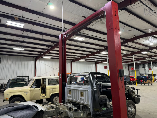 Auto repair shop with two lifted vehicles under red hydraulic lift posts