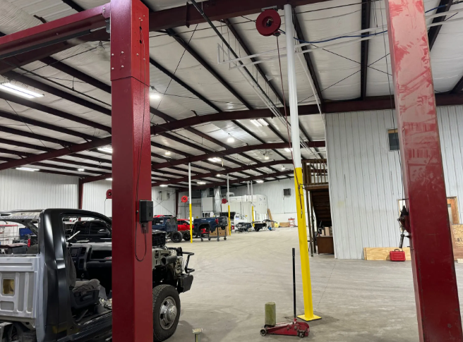Auto repair shop interior with red steel columns, a black truck, and a yellow lift pole on a concrete floor