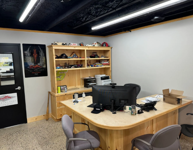 Office reception area with desk, chairs, computer monitors, shelves, and black ceiling beams