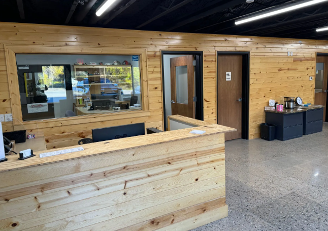 Wood-paneled office lobby with a front desk, window, open door, and speckled floor.