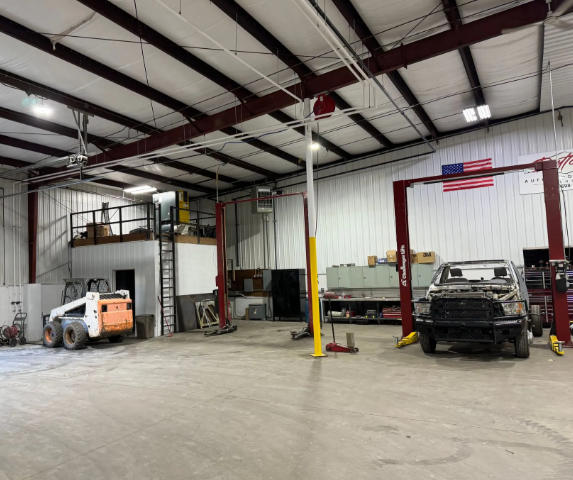 Industrial garage interior with trucks, a lift, and a mezzanine office under a high metal ceiling