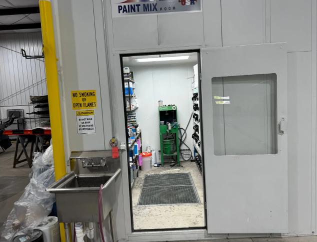 Industrial paint mixing room with open door, sink, and green equipment inside