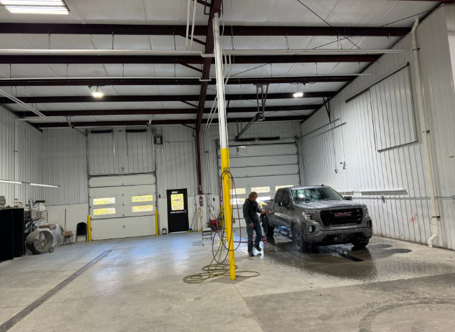 Two people beside a gray pickup truck inside a large industrial garage