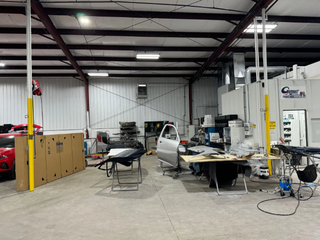 Warehouse workshop with car, worktables, tools, and equipment under metal ceiling lights