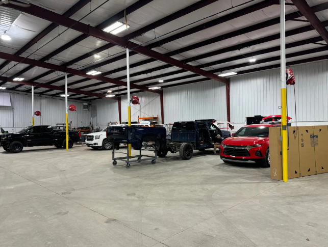 Spacious auto shop with several parked sports cars and trucks under bright overhead lights