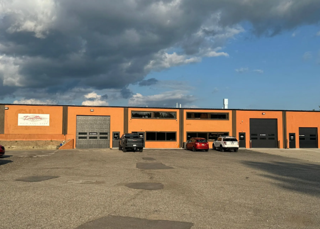 Orange industrial building with parked cars under a cloudy sky
