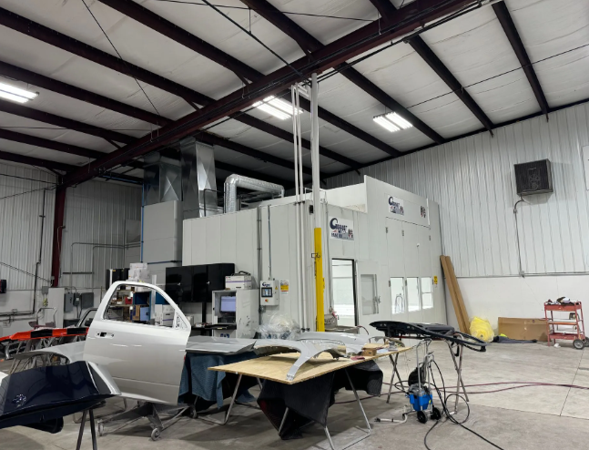 Auto body shop with a white car and disassembled parts inside a large industrial workshop.