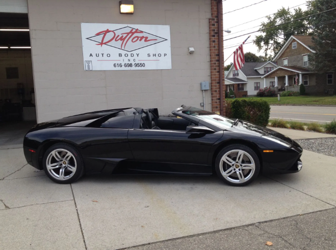 Black convertible sports car parked outside an auto body shop
