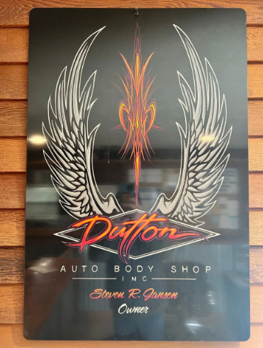 Black glossy sign with silver wings and red “Dutton” logo for an auto body shop