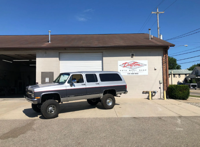 Lifted black-and-silver SUV parked outside a beige auto shop on a sunny day