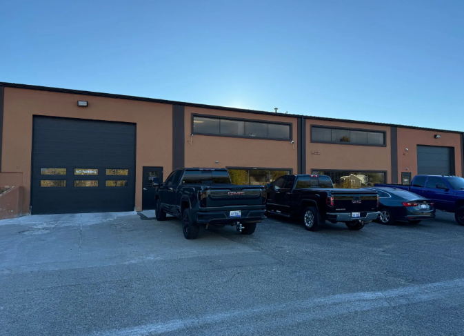 Brick industrial building with garage doors and several parked vehicles in front at dusk