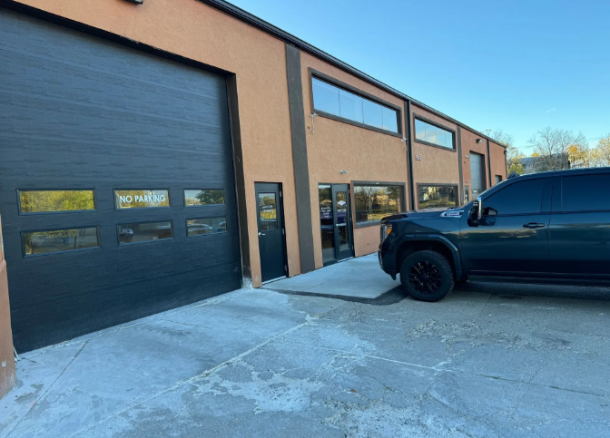 Commercial building with garage doors and a black truck parked outside on a concrete lot