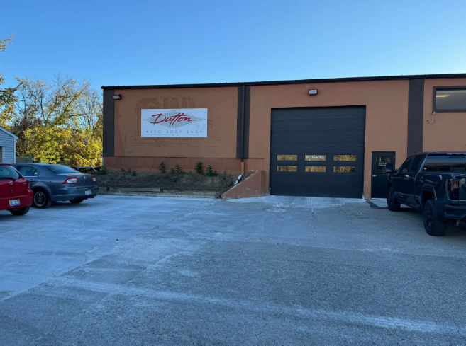 Industrial building with a large garage door, parked vehicles, and a sign on the front wall.