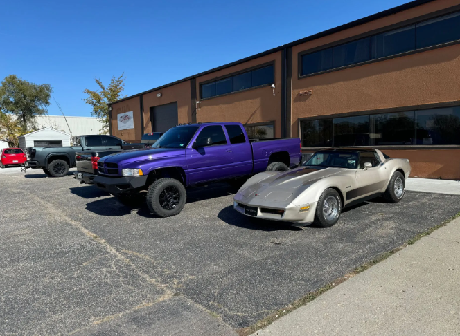 Purple pickup and silver sports car parked outside a brick building on a sunny day