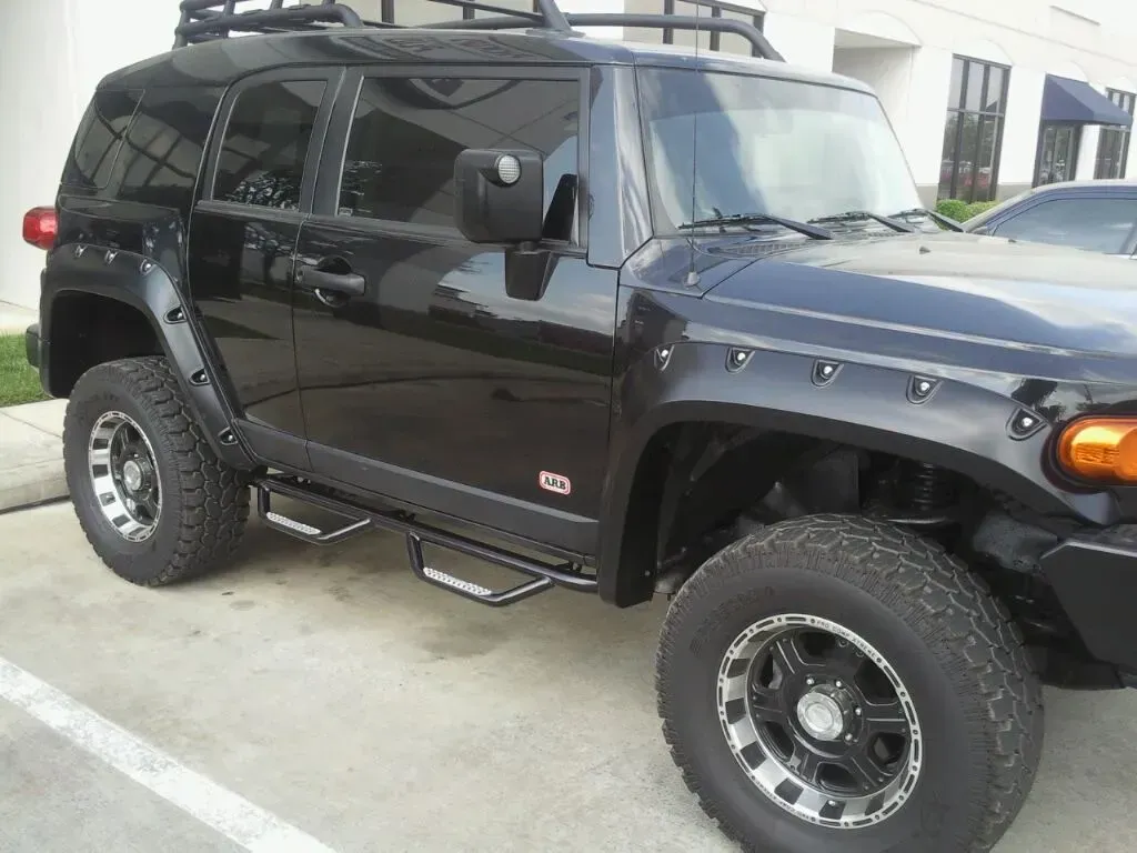 Black Toyota FJ Cruiser SUV with roof rack and step bars, parked.