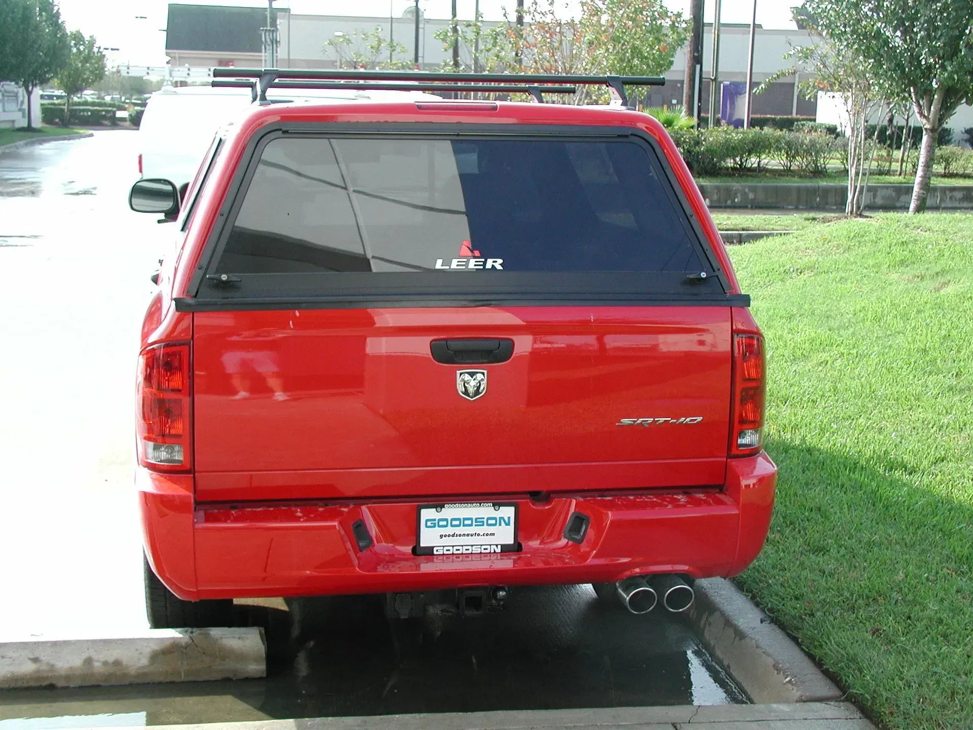 Red Dodge truck with a black camper shell and roof rack, parked in a parking lot.