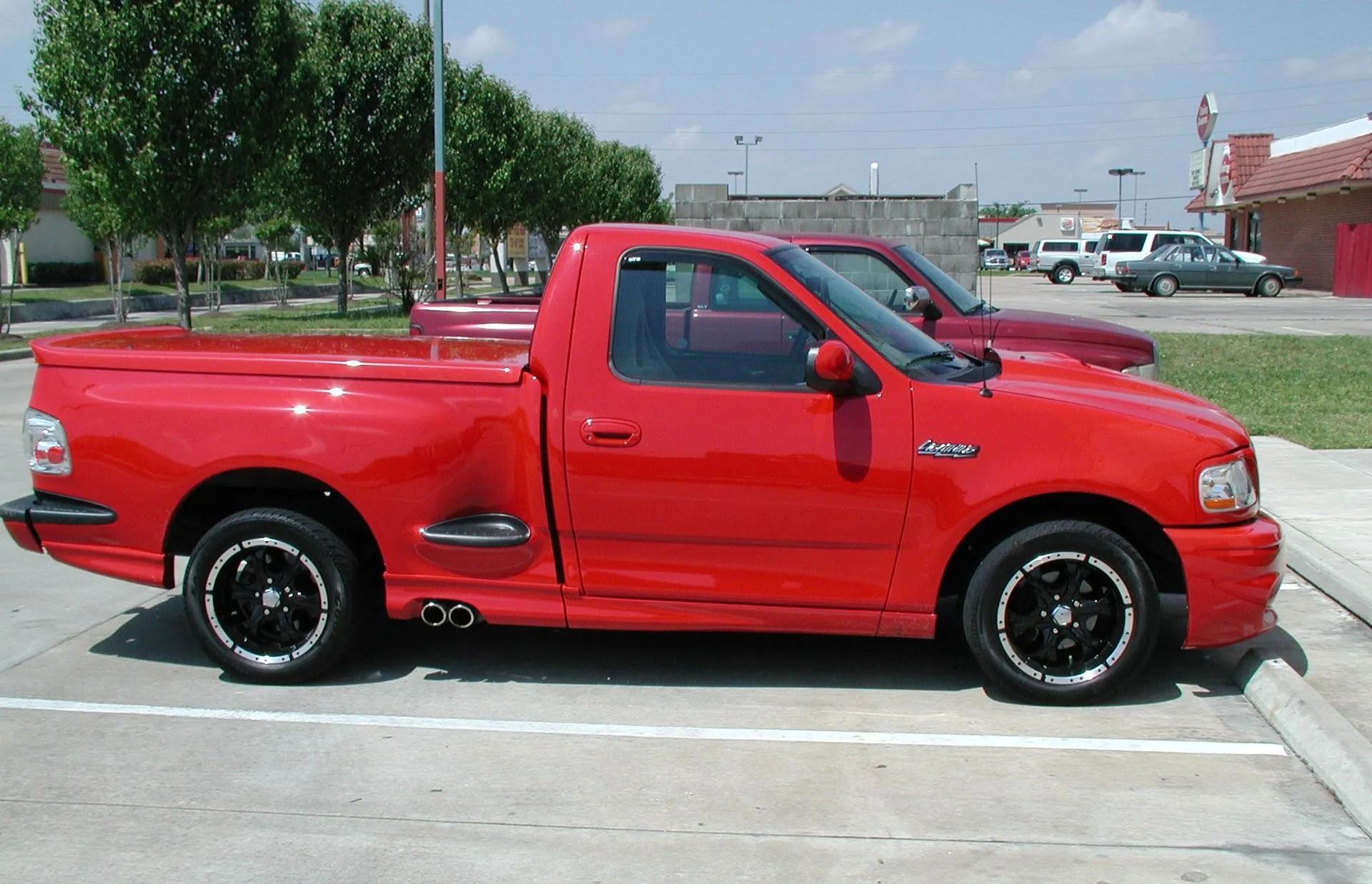 Red Ford F-150 Lightning pickup truck parked on concrete, black wheels, side exhaust.