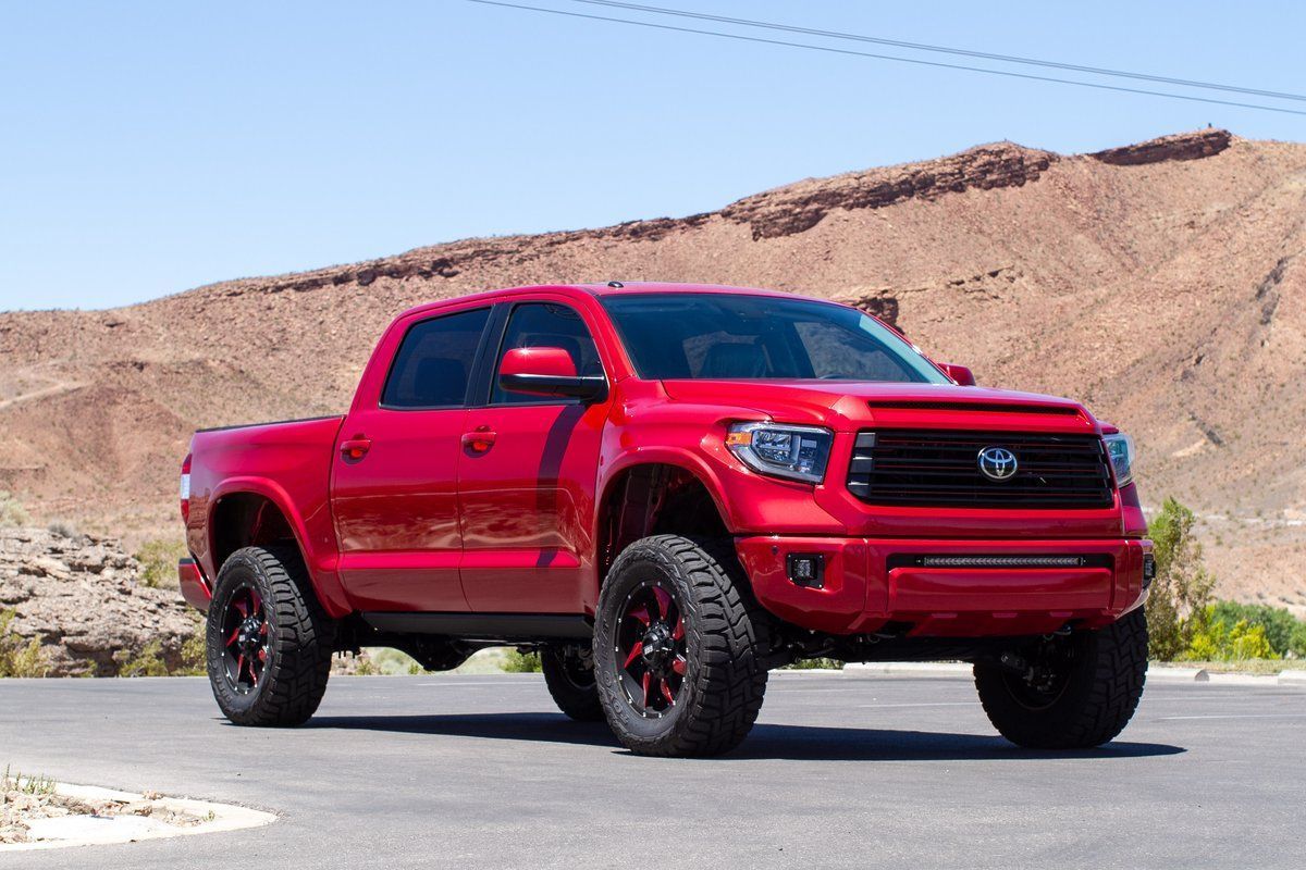 Red lifted Toyota Tundra truck on a paved road, in front of a tan mountain backdrop.