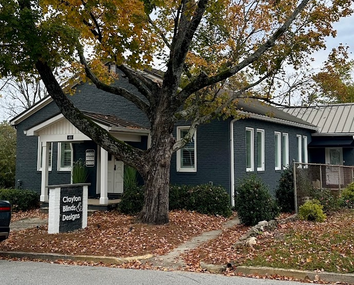 Dark blue building with white trim, Clayton Mills & Company sign, tree with fall foliage.